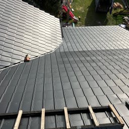 BYX-DACH Przemysław Byczyński - Nowe, grafitowe pokrycie dachowe z blachy trapezowej, częściowo zamontowane, z widocznym oknem dachowym i elementami konstrukcji drewnianej. Widok z góry.