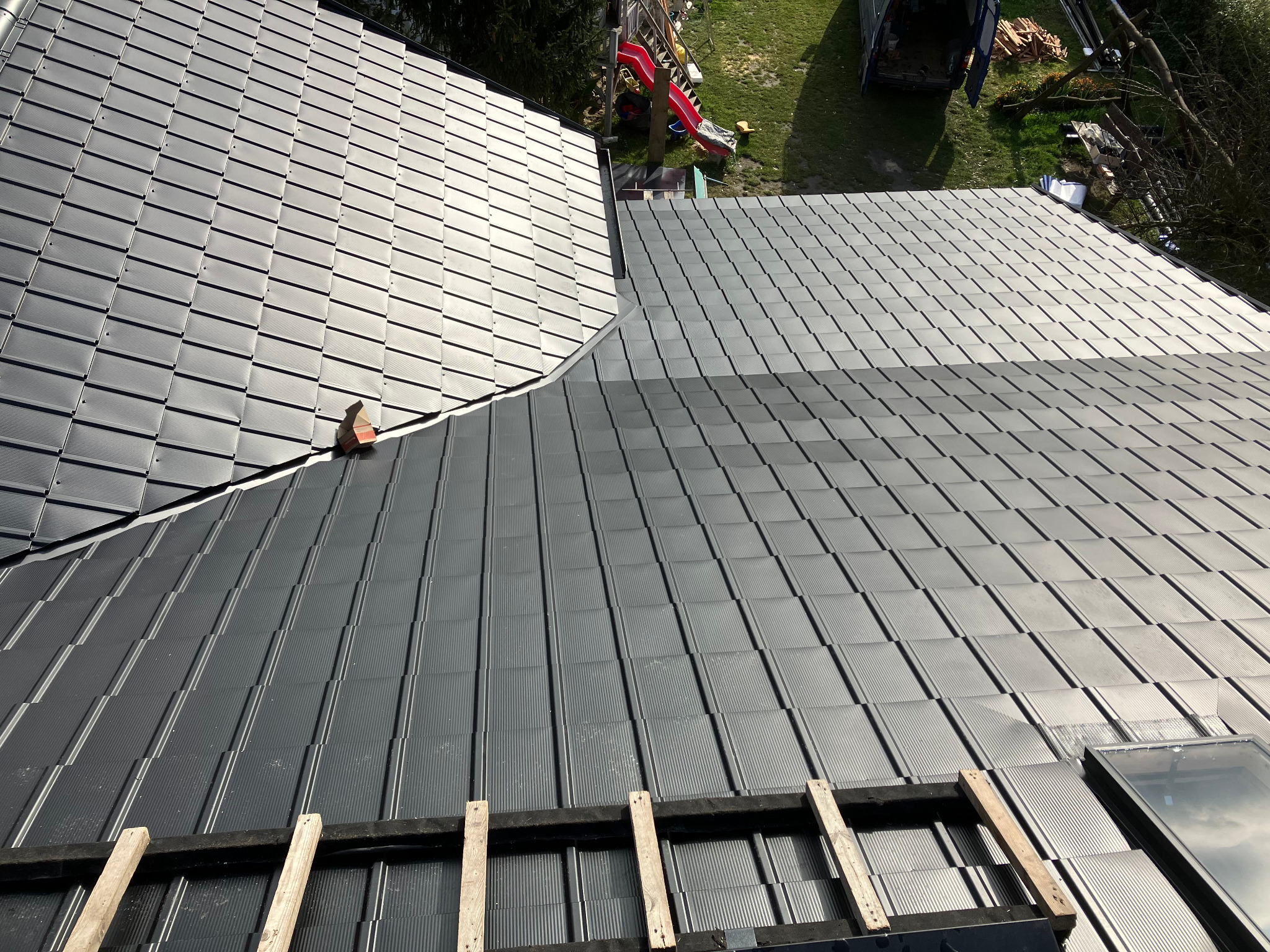 Nowe, grafitowe pokrycie dachowe z blachy trapezowej, częściowo zamontowane, z widocznym oknem dachowym i elementami konstrukcji drewnianej. Widok z góry.