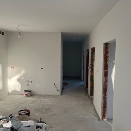 Zav-Bud - Wnętrze w trakcie prac wykończeniowych: świeżo pomalowane ściany na biało, widoczne puszki elektryczne, surowy beton na podłodze i przygotowane ościeżnice.