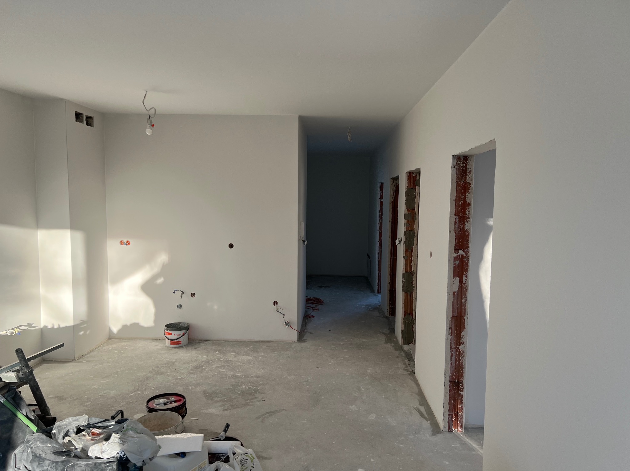 Wnętrze w trakcie prac wykończeniowych: świeżo pomalowane ściany na biało, widoczne puszki elektryczne, surowy beton na podłodze i przygotowane ościeżnice.