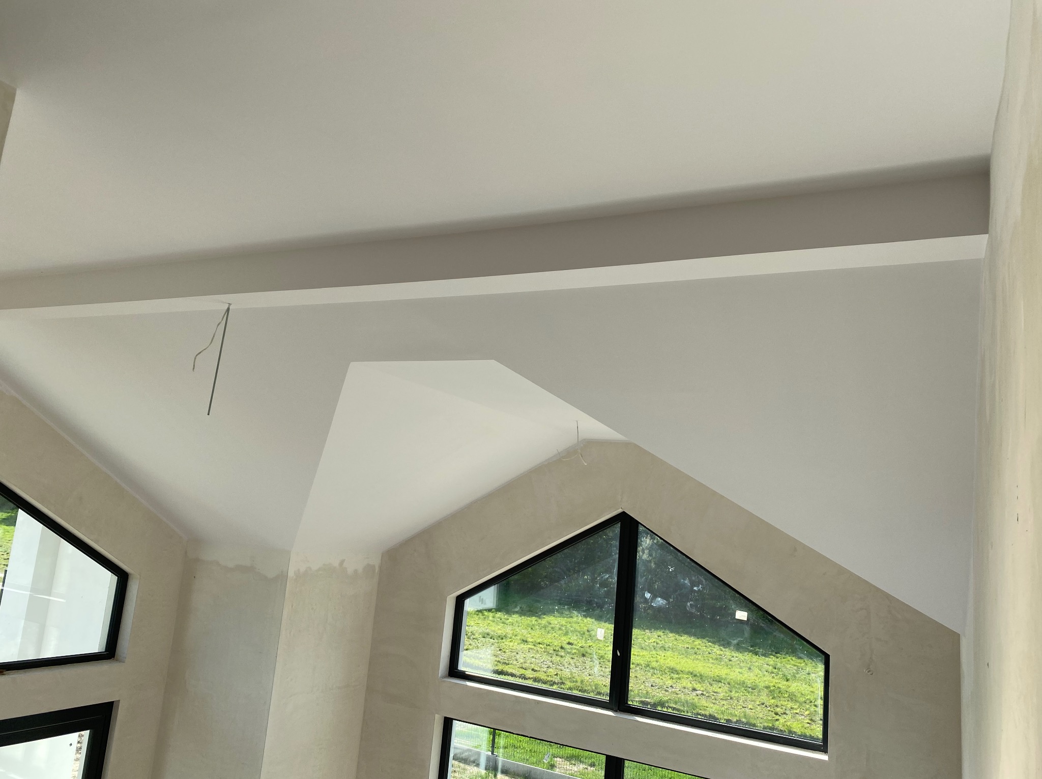 Wnętrze z wysokim sufitem i oknami trójkątnymi. Ściany w jasnym odcieniu, przygotowane do malowania. Widoczne niedoskonałości powierzchni przed wykończeniem.