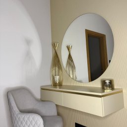 Meble na wymiar - Beżowa toaletka z okrągłym lustrem i złotymi akcentami, uzupełniona dekoracyjnymi wazonami i szarym krzesłem. Nowoczesny design z ryflowanym panelem ściennym.