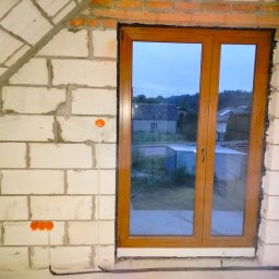 WJK Energia Wojciech Kubecki - Surowy stan poddasza z oknem i widocznymi puszkami instalacji elektrycznej w ścianie z betonu komórkowego. Widoczne przewody elektryczne.