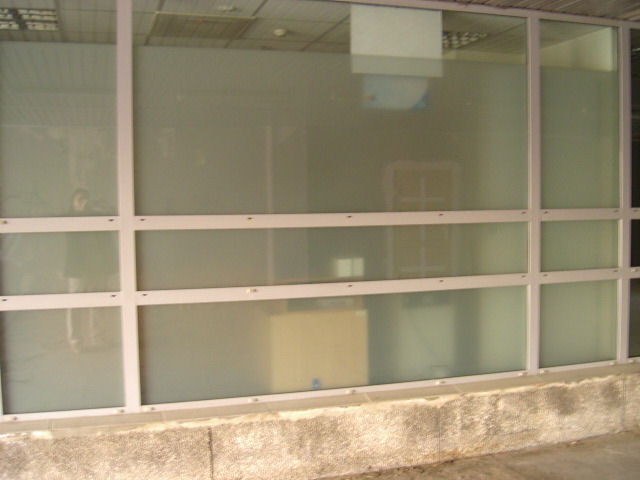 Okna biurowe z przyciemnioną folią, widoczne odbicia wnętrza pomieszczenia i fragment betonowej podstawy.