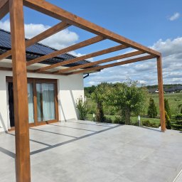 Timberview - Nowoczesna pergola z drewna na tarasie z szarych płyt, z widokiem na ogród i dom z panelami słonecznymi. Jasne, słoneczne oświetlenie.
