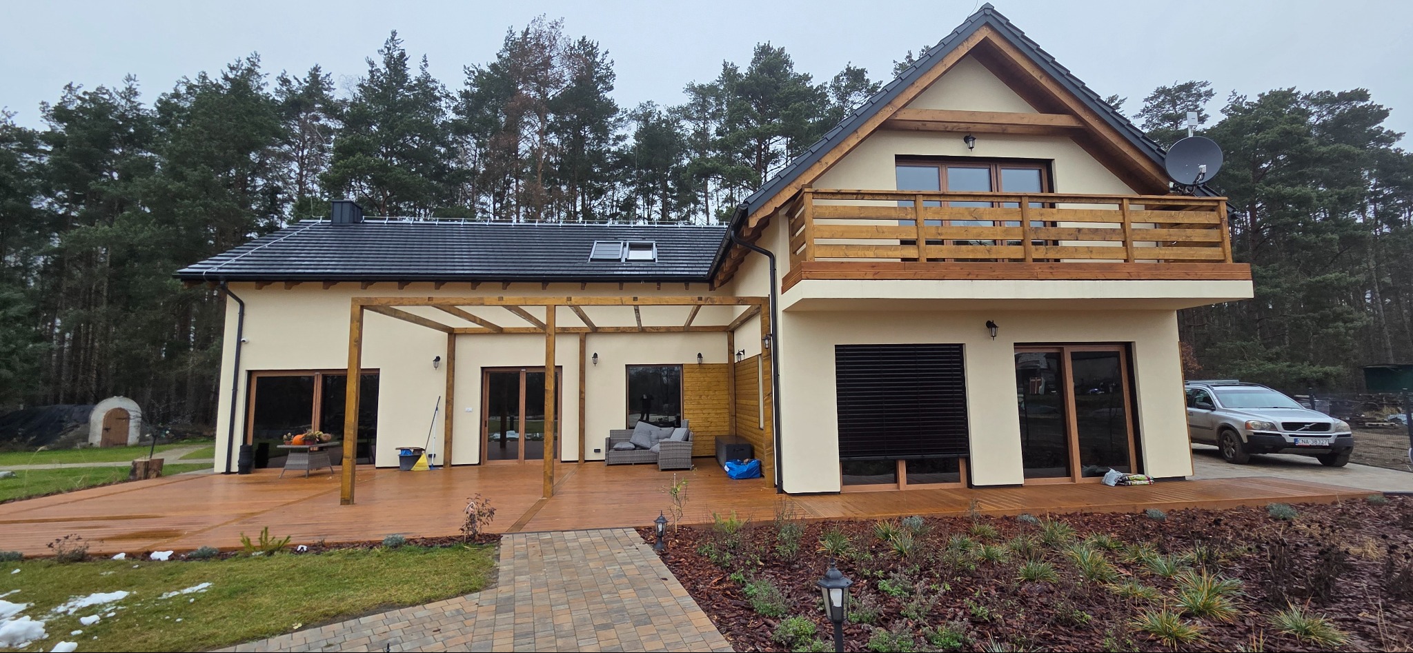 Nowoczesny dom z drewnianym tarasem i pergolą. Balustrada z drewna na balkonie. Uwagę przyciąga starannie wykonana nawierzchnia tarasu i dopasowana pergola.