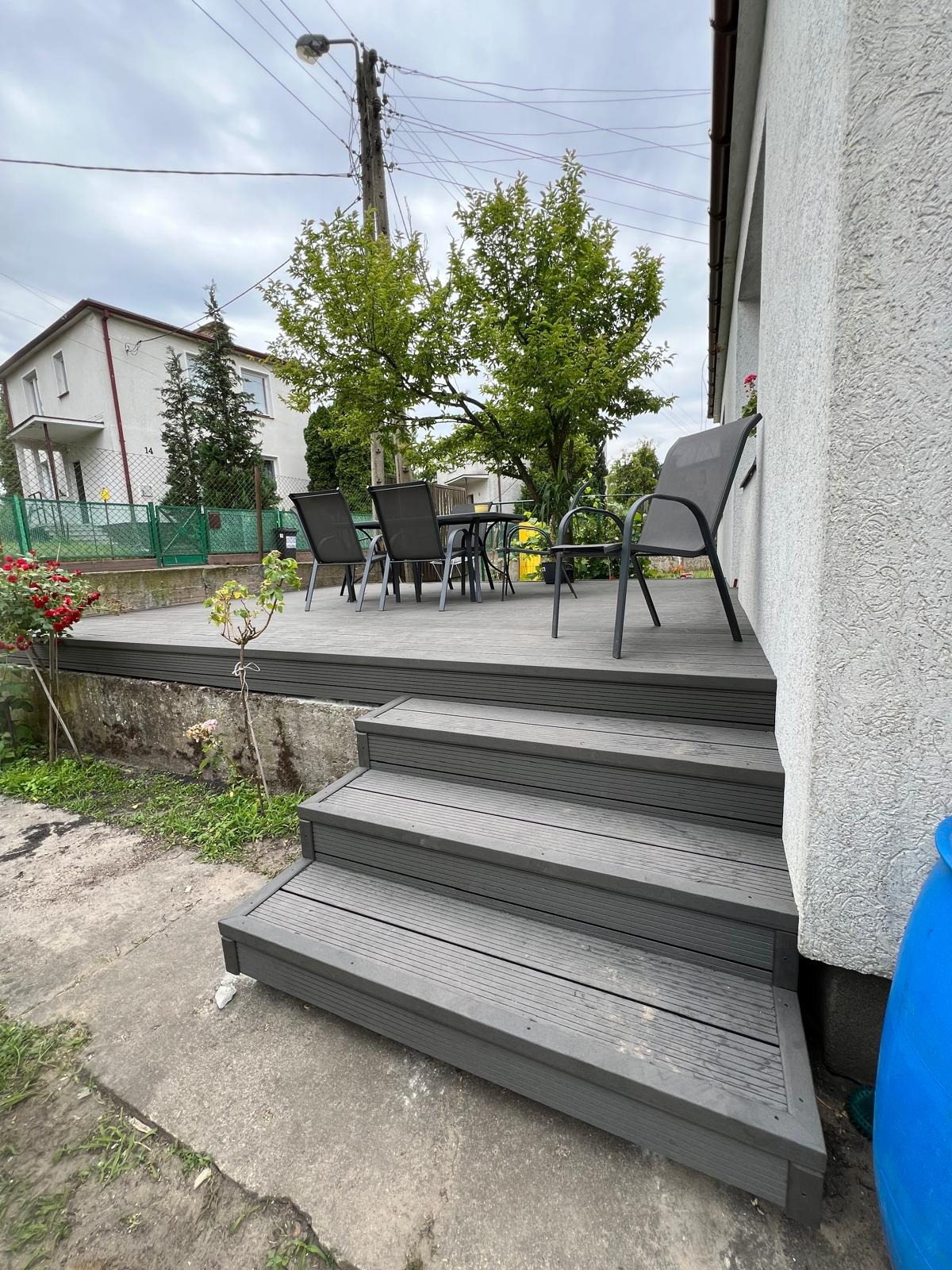 Szary taras kompozytowy z trzema schodami, zestawem mebli ogrodowych i widokiem na dom w tle, wykonany w pochmurny dzień.