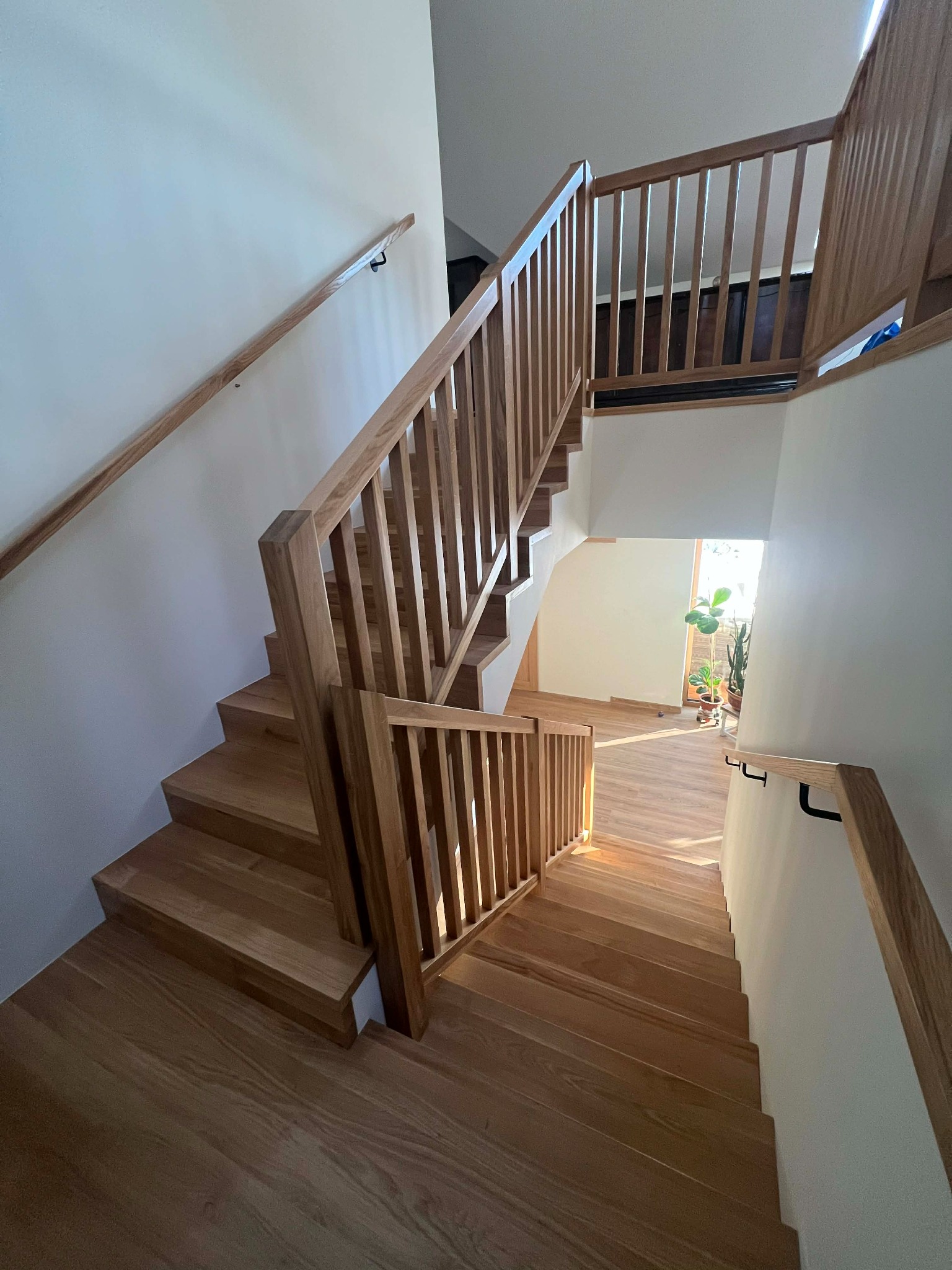 Jasne, drewniane schody z balustradą w nowoczesnym wnętrzu. Widok z góry, naturalne światło podkreśla strukturę drewna. Minimalistyczny design, rośliny w tle.