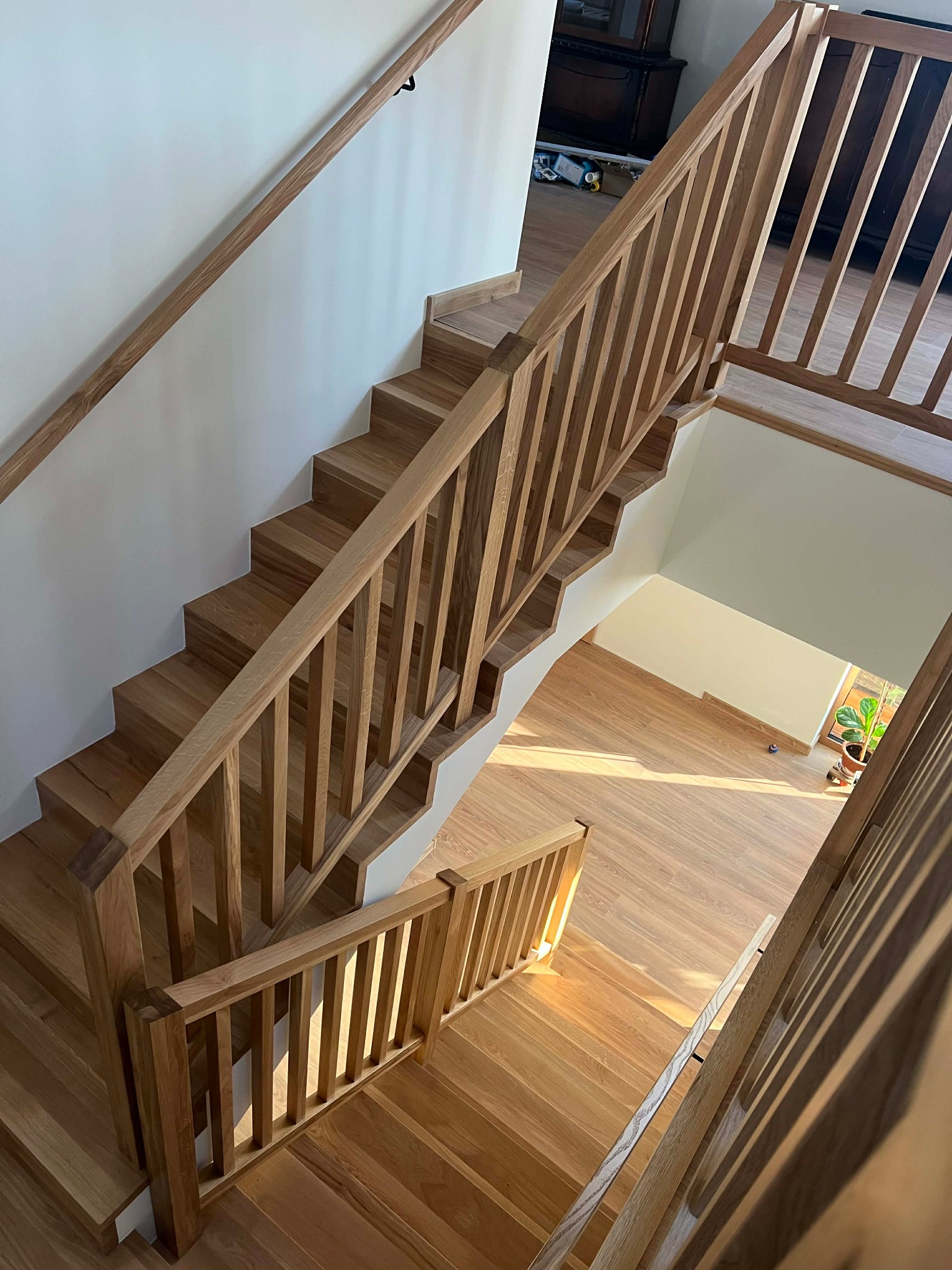 Jasne, drewniane schody z balustradą, widok z góry. Naturalne oświetlenie podkreśla strukturę drewna. Minimalistyczny design, białe ściany, drewniana podłoga na dole.