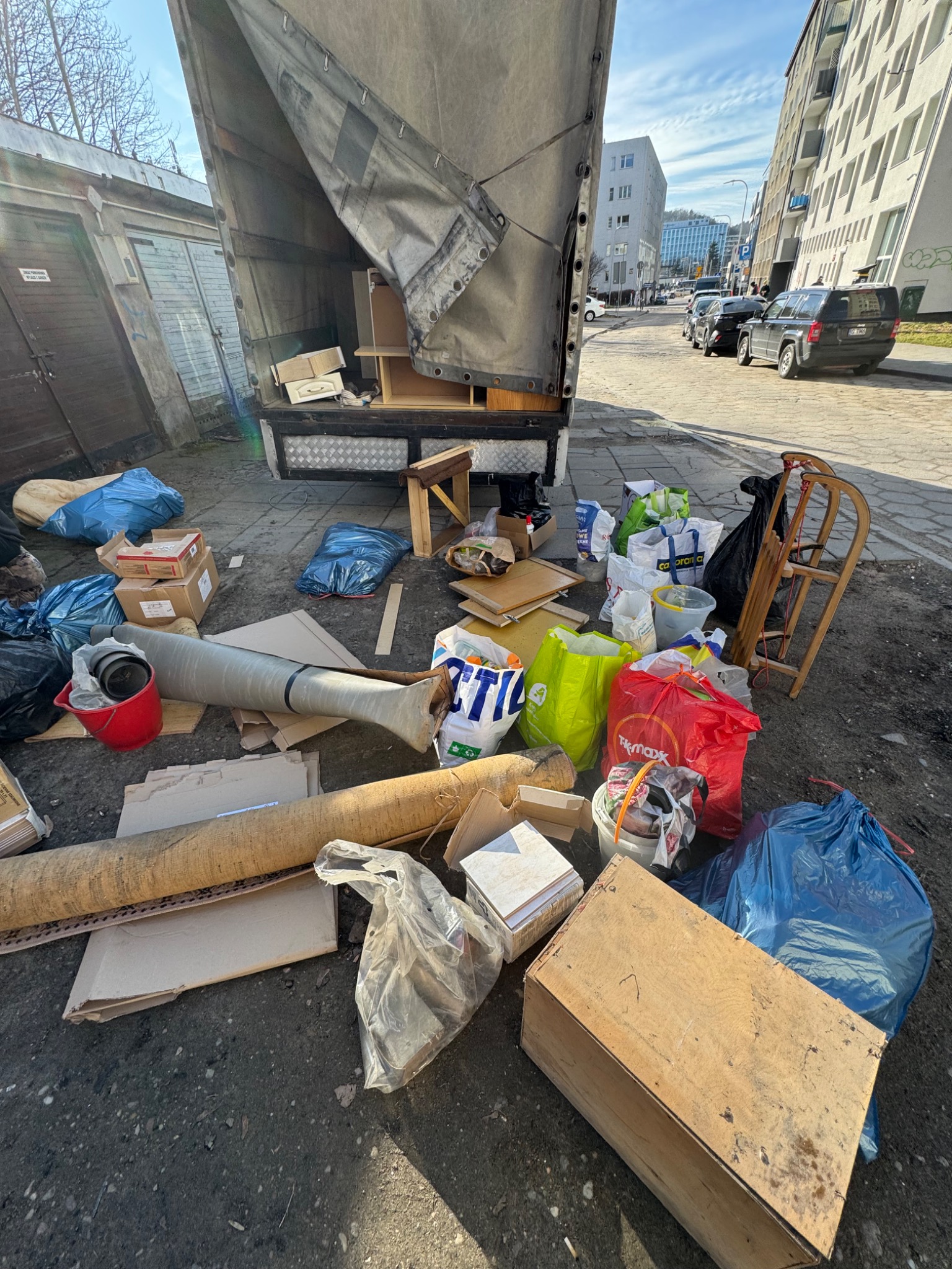 Opróżnianie mieszkania: Załadowany śmieciami i meblami samochód dostawczy na tle miejskiej zabudowy. Widoczne worki, kartony i inne przedmioty przeznaczone do utylizacji.