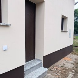 B&K FLEX SP. Z O.O. - Elewacja domu po malowaniu w odcieniach beżu i brązu, z granitowymi schodami wejściowymi. Widoczny fragment okna i drzwi wejściowych. Detal wykończenia.