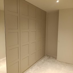 B&K FLEX SP. Z O.O. - Beżowa zabudowa szafy wnękowej z lustrem na boku, widoczna w surowym stanie pomieszczenia. Minimalistyczny design, ciepłe oświetlenie sufitowe.