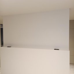B&K FLEX SP. Z O.O. - Gładka, świeżo pomalowana ściana w jasnym odcieniu bieli, z widocznymi śladami po taśmie malarskiej na dolnej części. Minimalistyczne wnętrze w trakcie wykończenia.