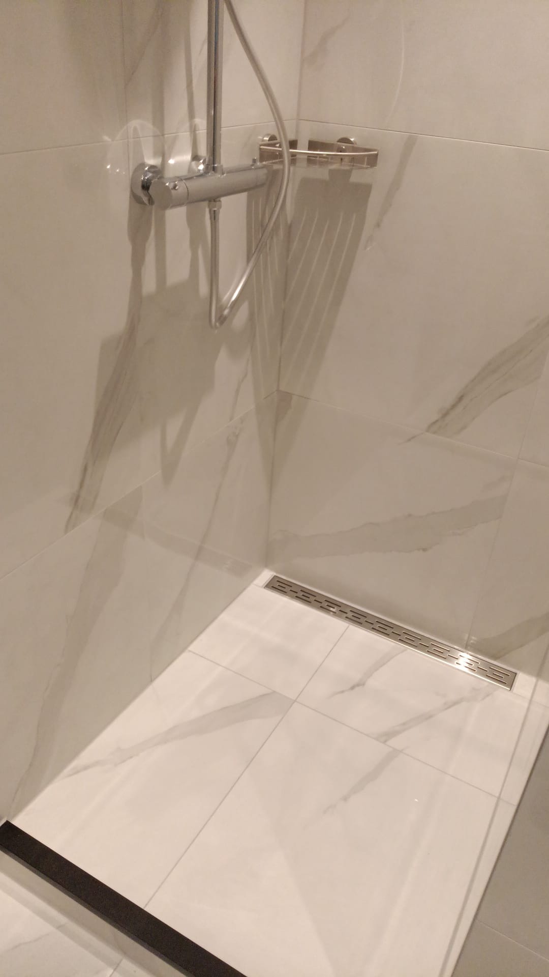 Nowoczesny prysznic walk-in z odpływem liniowym i marmurowymi płytkami. Chromowana armatura i minimalistyczny design. Widok z góry, podkreślający detale wykończenia.