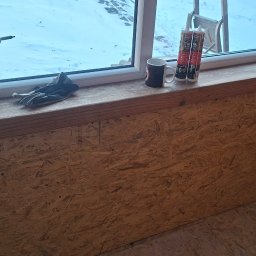 Laki - Wnętrze w trakcie wykańczania płytami OSB, widoczna wiertarka, rękawice robocze, puszki z uszczelniaczem i kubek na parapecie okna. Prace wykończeniowe.