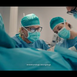 Michał Janicki - Kadr z filmu: zespół chirurgów w trakcie operacji tarczycy, w zielonych strojach i maskach, skupiony na zabiegu. Oświetlenie studyjne, precyzyjne ujęcie.