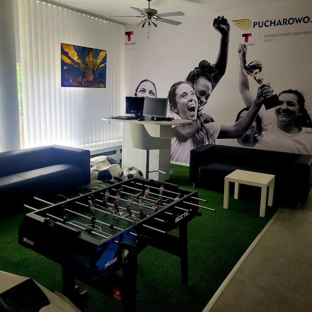 Nowoczesne biuro z piłkarzykami, sofami i grafiką ścienną z motywem sportowym. Wyjątkowa aranżacja przestrzeni biurowej z elementami rekreacyjnymi i wizualizacją marki.