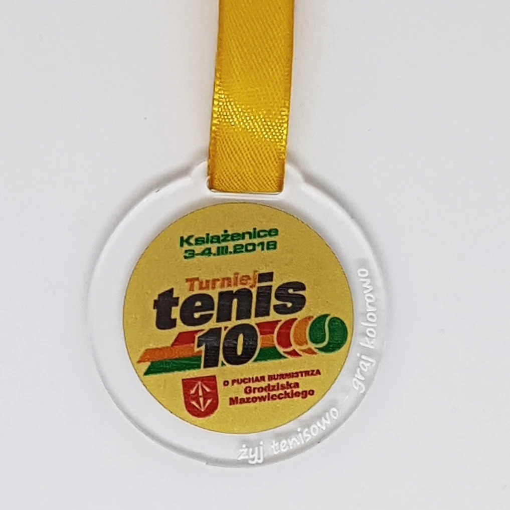 Przezroczysty medal z żółtą wstążką, upamiętniający turniej tenisowy 'Tenis 10' w Książenicach, z datą 3-4.11.2018 i herbem Grodziska Mazowieckiego.