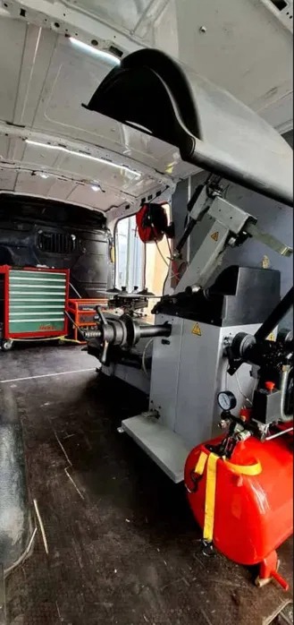 Wnętrze mobilnego warsztatu wulkanizacyjnego w busie: wyważarka do kół, czerwony kompresor i wózek narzędziowy. Gotowość do serwisu opon w terenie.