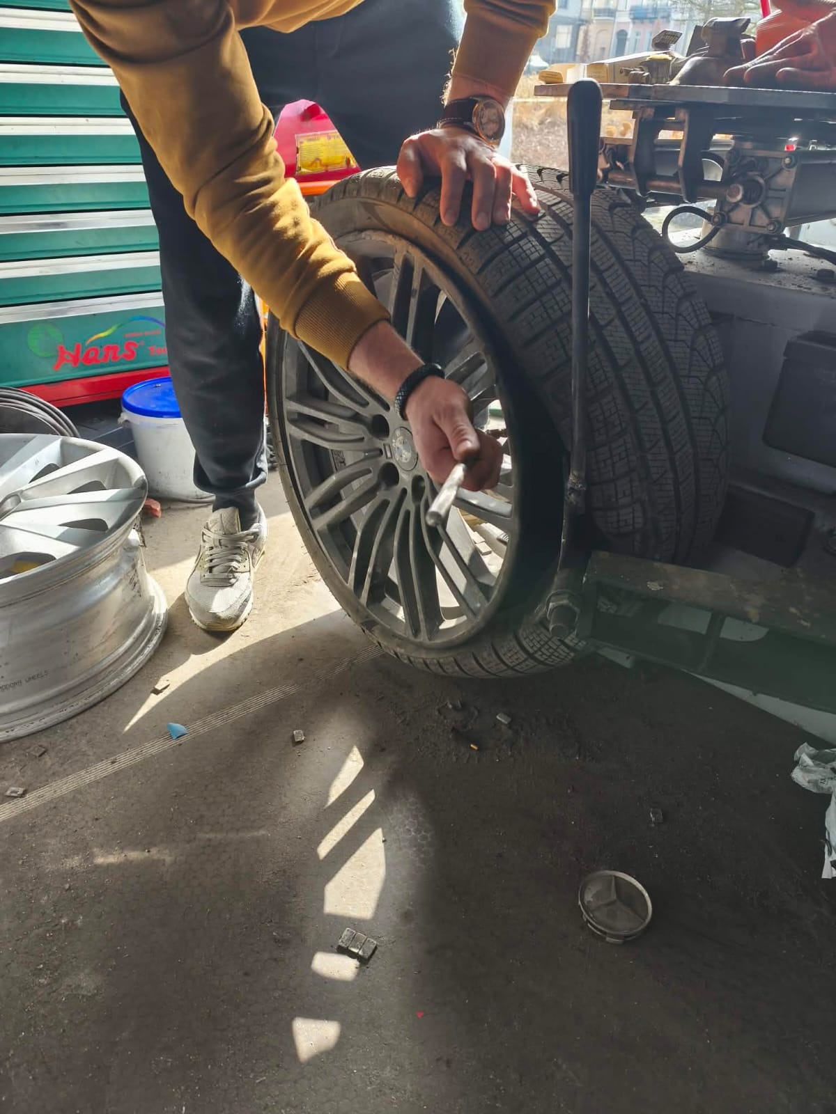 Wulkanizacja mobilna: mężczyzna demontuje oponę zimową z felgi aluminiowej za pomocą łyżki montażowej. Widoczne ciężarki do wyważania kół.