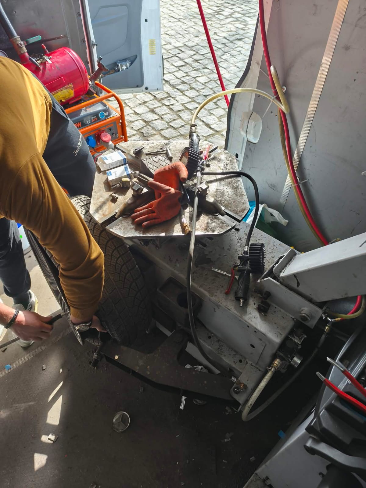 Wulkanizacja mobilna w trakcie pracy: opona na maszynie, narzędzia, rękawice robocze, kompresor wewnątrz busa. Usługa dostępna 24/7.