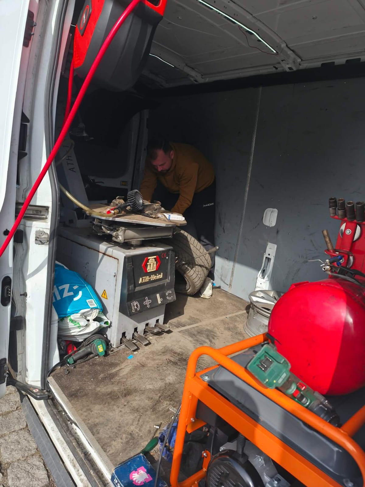 Wnętrze mobilnego warsztatu wulkanizacyjnego w busie: mechanik przy maszynie do opon, kompresor, narzędzia. Serwis opon w trasie.