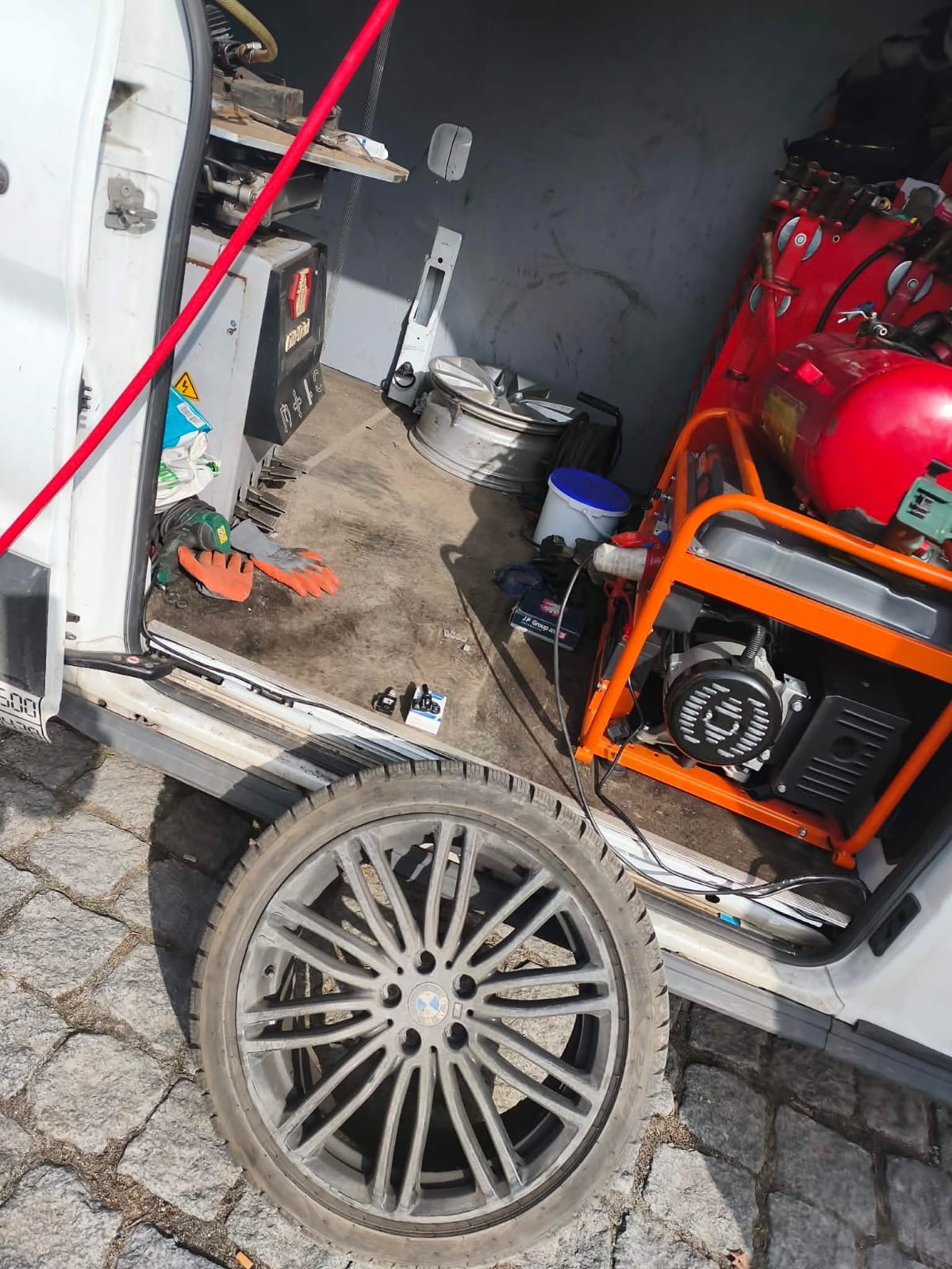 Wnętrze mobilnego warsztatu wulkanizacyjnego: koło z felgą BMW na pierwszym planie, w tle agregat prądotwórczy i narzędzia w busie.