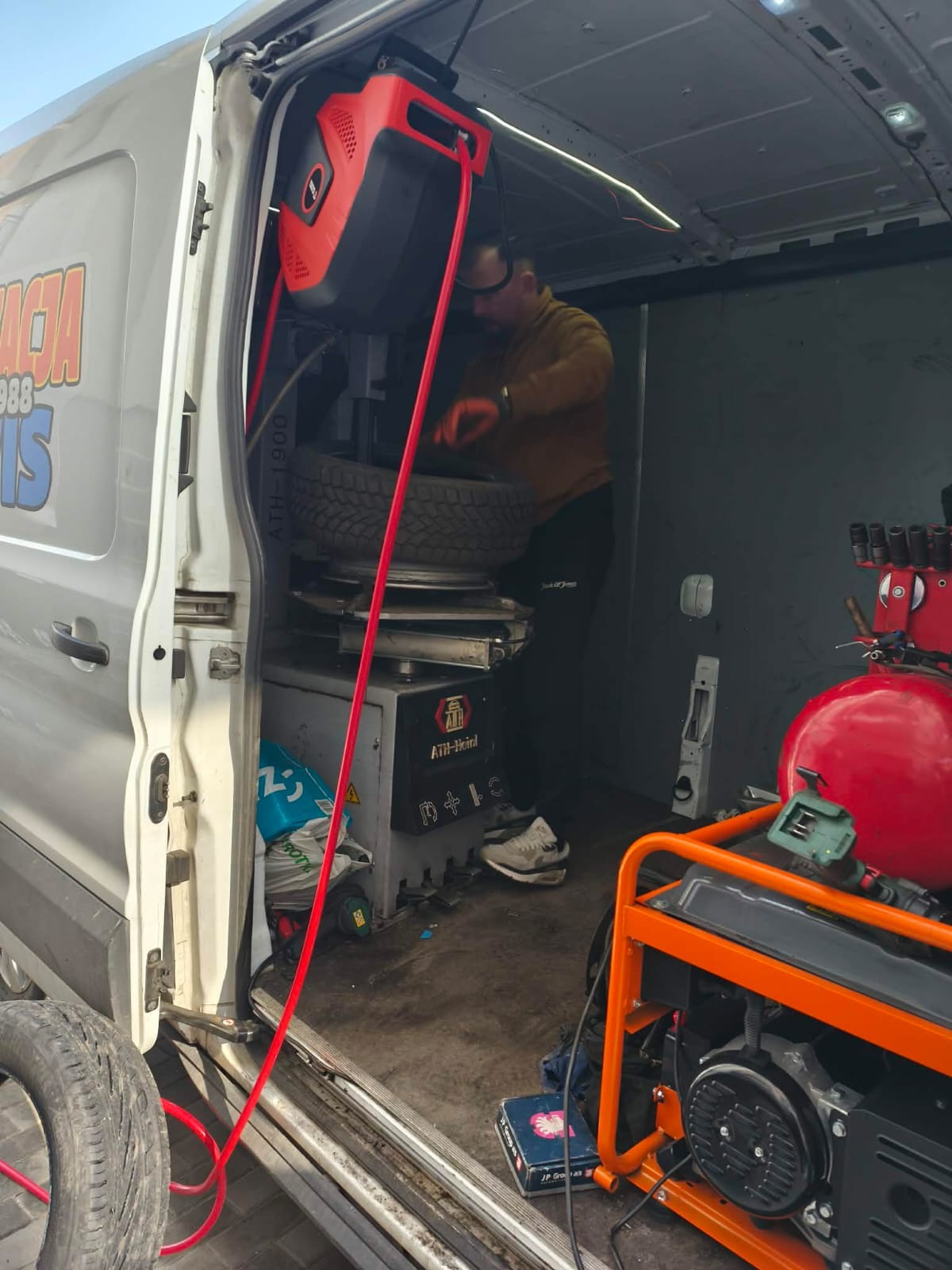 Mobilny serwis opon: mechanik w busie wulkanizacyjnym wymienia oponę na montażownicy ATH-1900. Widoczny agregat prądotwórczy i kompresor.