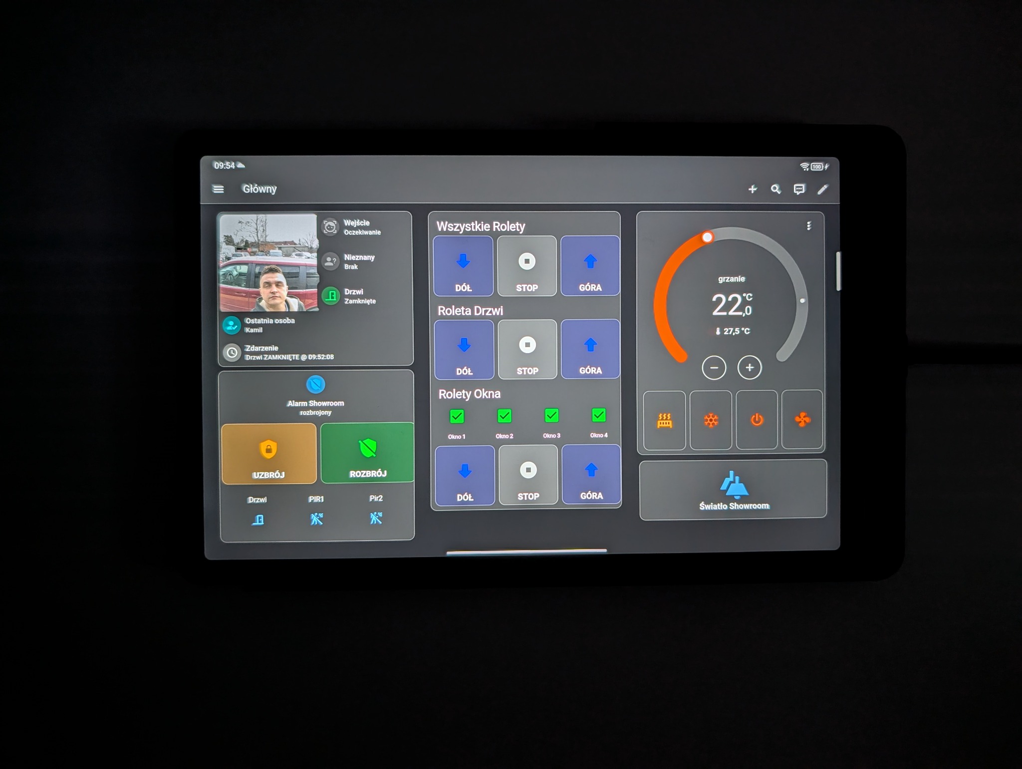 Tablet z interfejsem sterowania inteligentnym domem: rolety, ogrzewanie, alarm. Widok z bliska na ekran z elementami sterującymi i informacjami o stanie systemu.