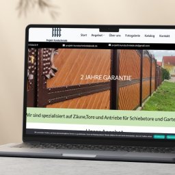 NiuBrands Marceli Ratajczak - Laptop wyświetla stronę internetową firmy Projekt-Kunstschmiede z ofertą bram i ogrodzeń. Cień roślin na ścianie, neutralne tło. Widok z boku, lekki kąt.