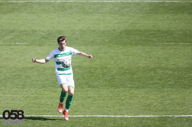 Młody mężczyzna w sportowym stroju z piłką na boisku w Łodzi. Dynamiczne ujęcie, trening piłkarski na tle zielonej trawy i białych linii.