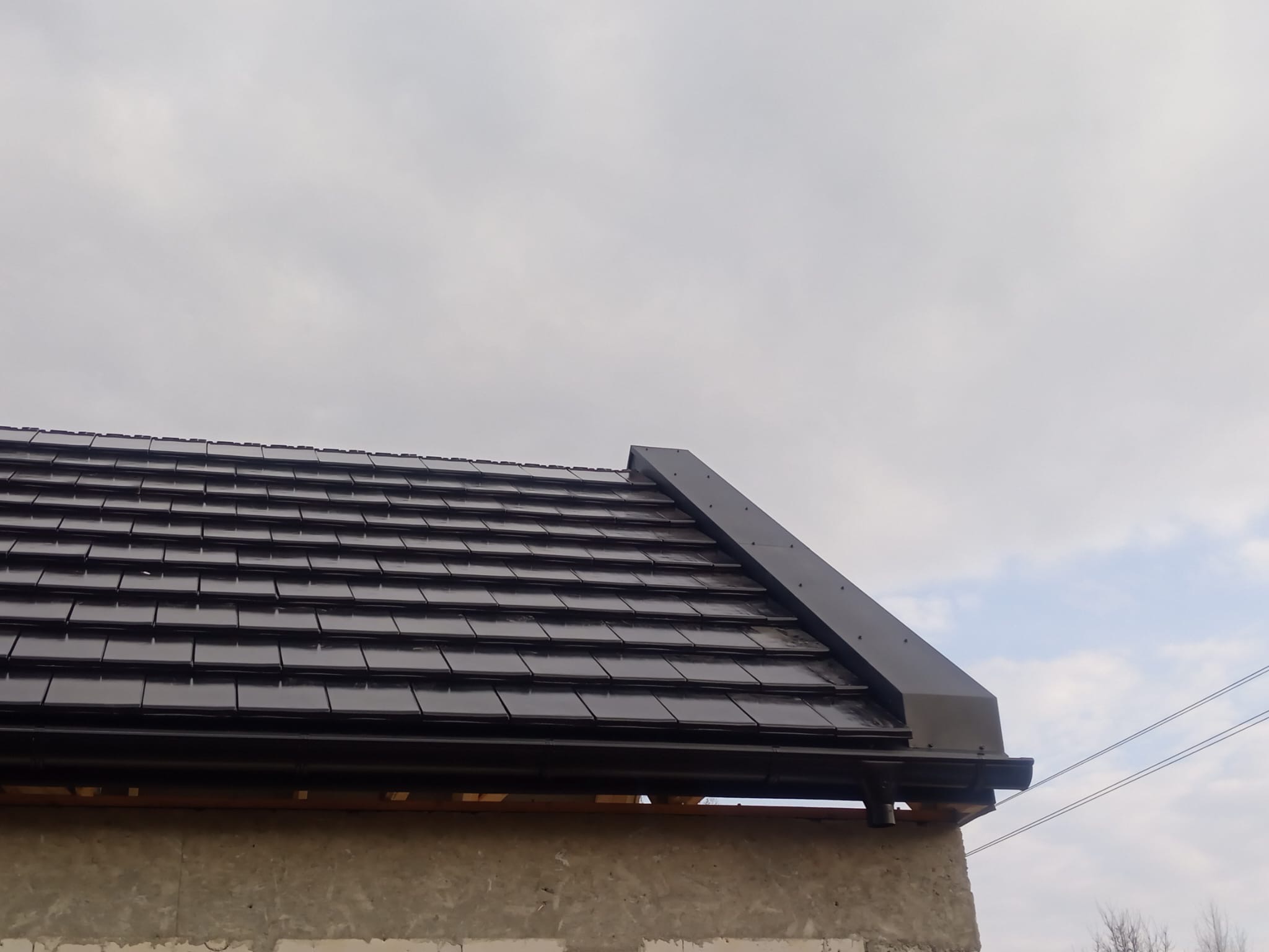 Ciemna dachówka ceramiczna na budynku w Lubomierzu, widok z dołu, ukazujący detale orynnowania i wykończenia dachu. Nowoczesne pokrycie.