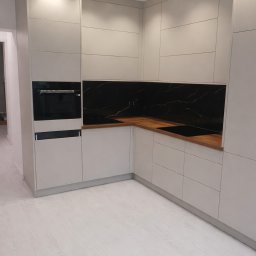 MIROSŁAW SKUBISZ - Jasna kuchnia na wymiar z drewnianym blatem i czarnym panelem. Minimalistyczny design, oświetlenie punktowe. Fronty szafek z delikatnym frezem.