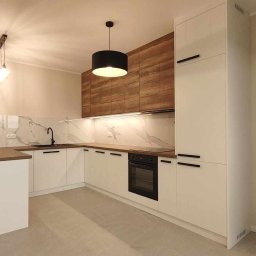 MIROSŁAW SKUBISZ - Nowoczesna kuchnia z białymi szafkami i drewnianymi akcentami. Marmurowy backsplash, czarne uchwyty i oświetlenie LED. Minimalistyczny design z wyspą.