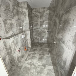Scarbud - Oskar Kolaska - Wykończona łazienka w szarościach w Starogardzie Gdańskim. Widoczne płytki imitujące beton, armatura i narzędzia glazurnicze. Minimalistyczny design, surowy styl.