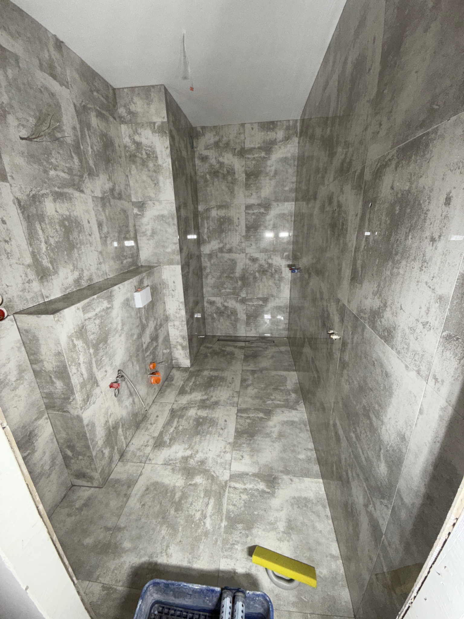 Wykończona łazienka w szarościach w Starogardzie Gdańskim. Widoczne płytki imitujące beton, armatura i narzędzia glazurnicze. Minimalistyczny design, surowy styl.