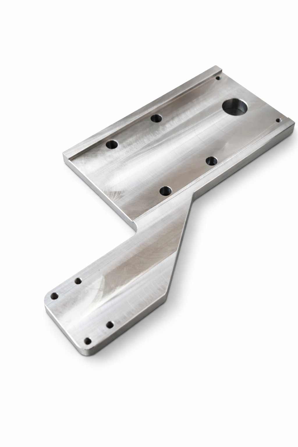 Precyzyjnie obrobiony, metalowy element z otworami, wykonany metodą CNC, leżący na białym tle. Widoczne ślady obróbki.