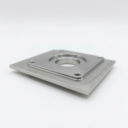 SON - MET PATRYK MORAWSKI - Precyzyjnie obrobiony, metalowy element o kwadratowej podstawie i centralnym, cylindrycznym otworem, widoczny na białym tle. Detal z czterema otworami na śruby.