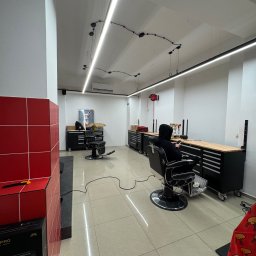 Usługi Elektryczne Maksymilian Lis - Nowoczesne oświetlenie LED w salonie fryzjerskim z czarnymi meblami warsztatowymi i klientem w fotelu. Minimalistyczny design z akcentami czerwieni.