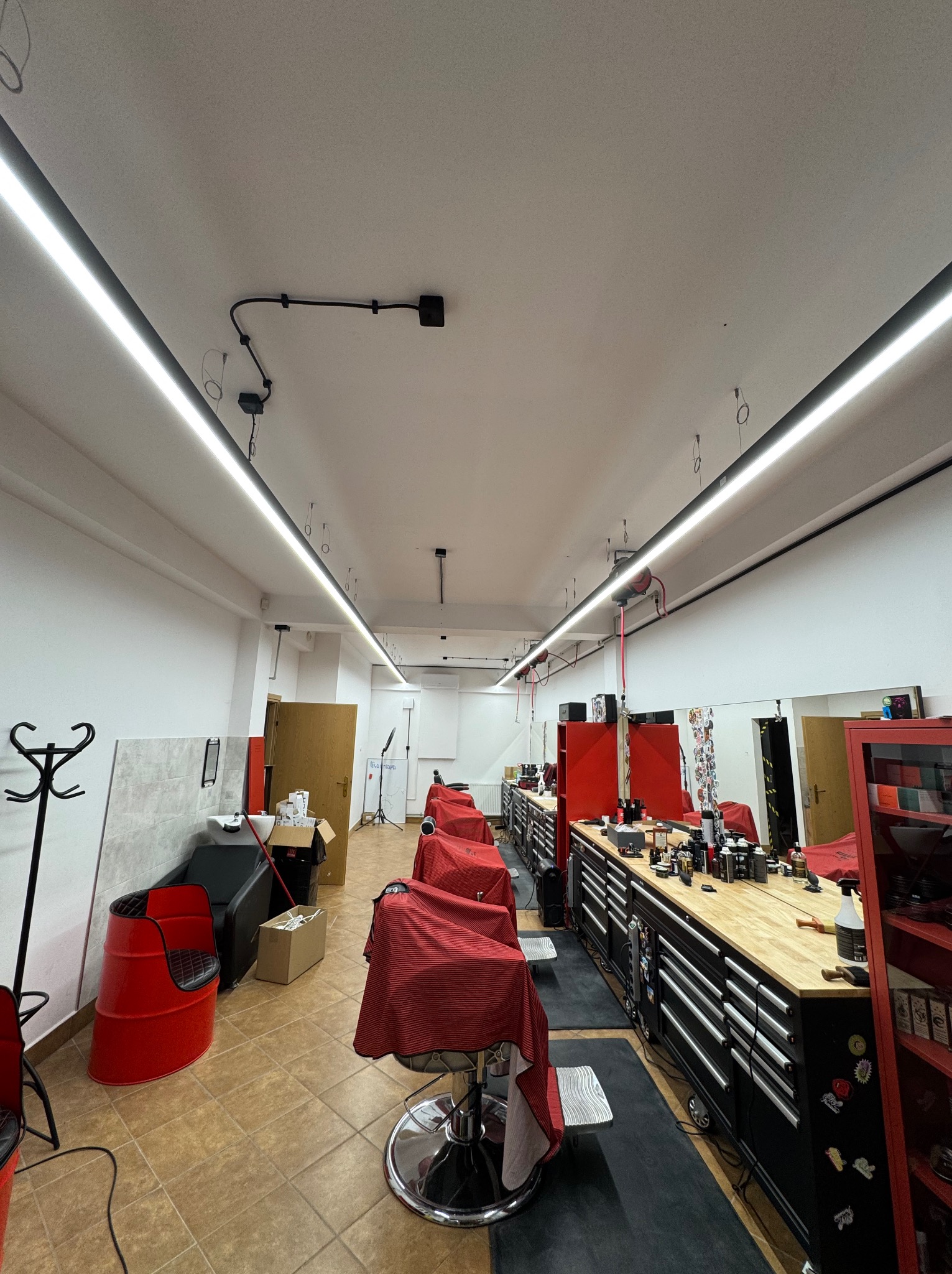 Wnętrze salonu fryzjerskiego z oświetleniem LED, stanowiskami pracy i czerwonymi akcentami. Widoczne narzędzia i wyposażenie fryzjerskie.