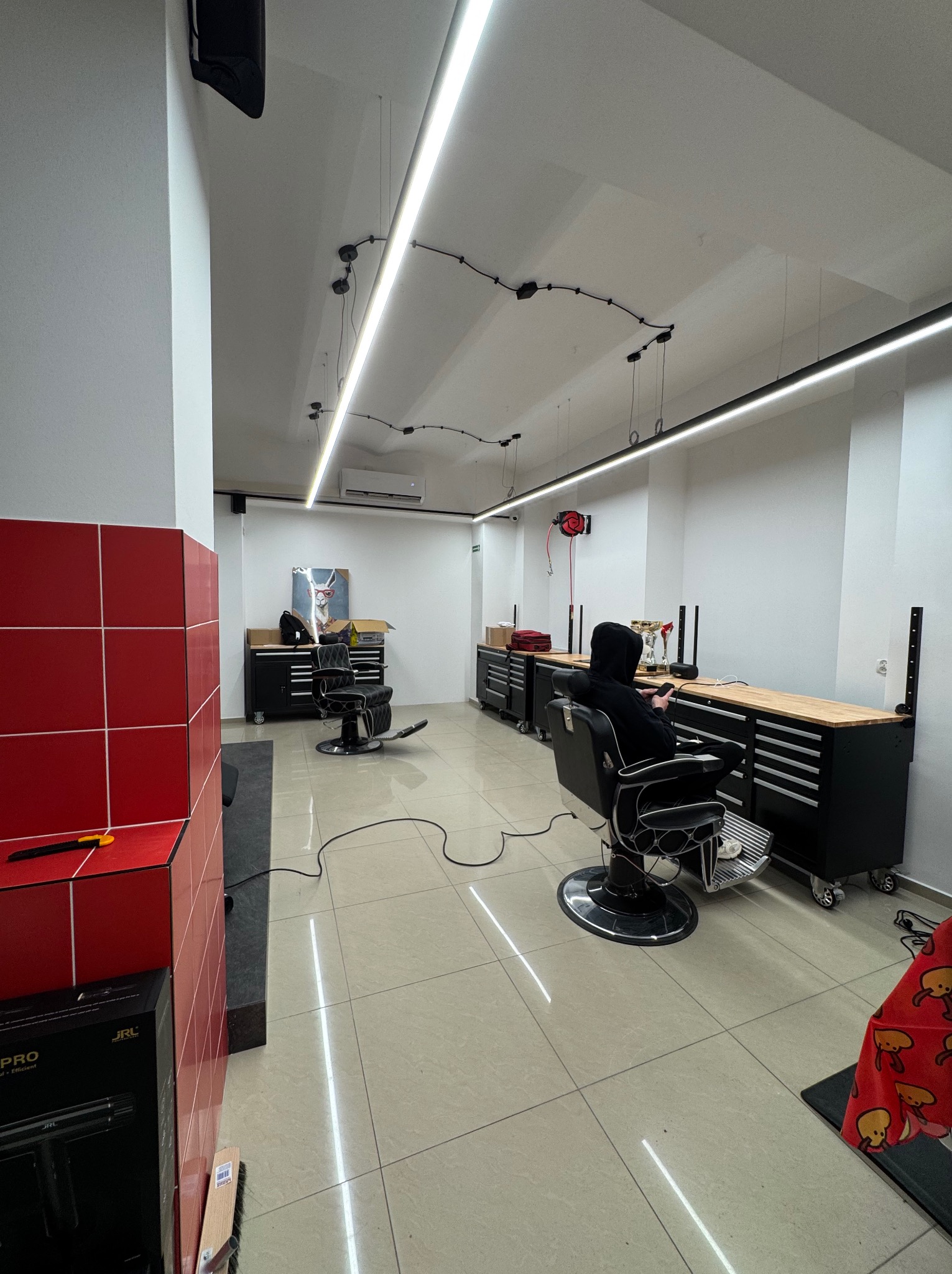 Nowoczesne oświetlenie LED w salonie fryzjerskim z czarnymi meblami warsztatowymi i klientem w fotelu. Minimalistyczny design z akcentami czerwieni.