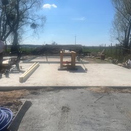 SIMS HOUSE SP. Z O. O. - Wylany fundament pod budowę domu jednorodzinnego, widoczne szalunki i przygotowane drewno konstrukcyjne. Słoneczny dzień, błękitne niebo.