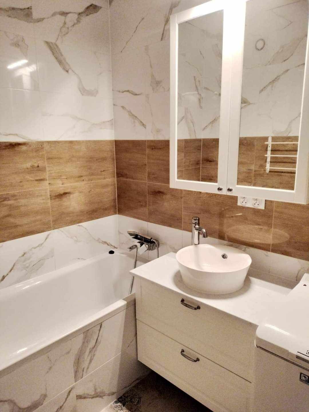 Nowoczesna łazienka z wanną, umywalką nablatową i lustrem w szafce. Płytki imitujące marmur i drewno. Armatura chromowana. Ujęcie z bliska, widok na detale.