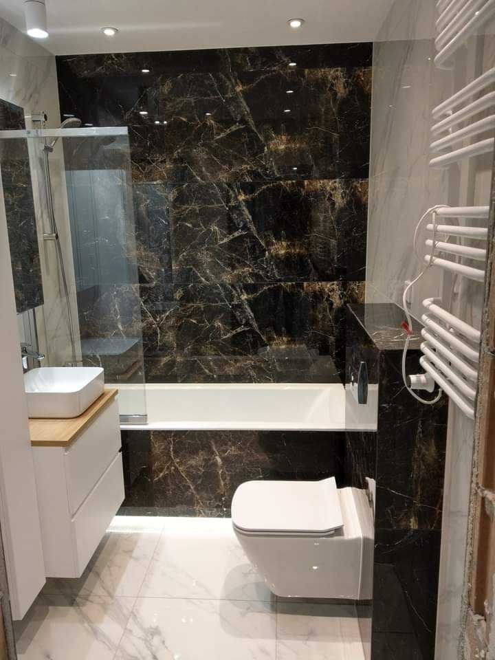 Elegancka łazienka z czarnymi płytkami imitującymi marmur, białą armaturą i kabiną prysznicową. Widoczne oświetlenie punktowe i grzejnik drabinkowy.