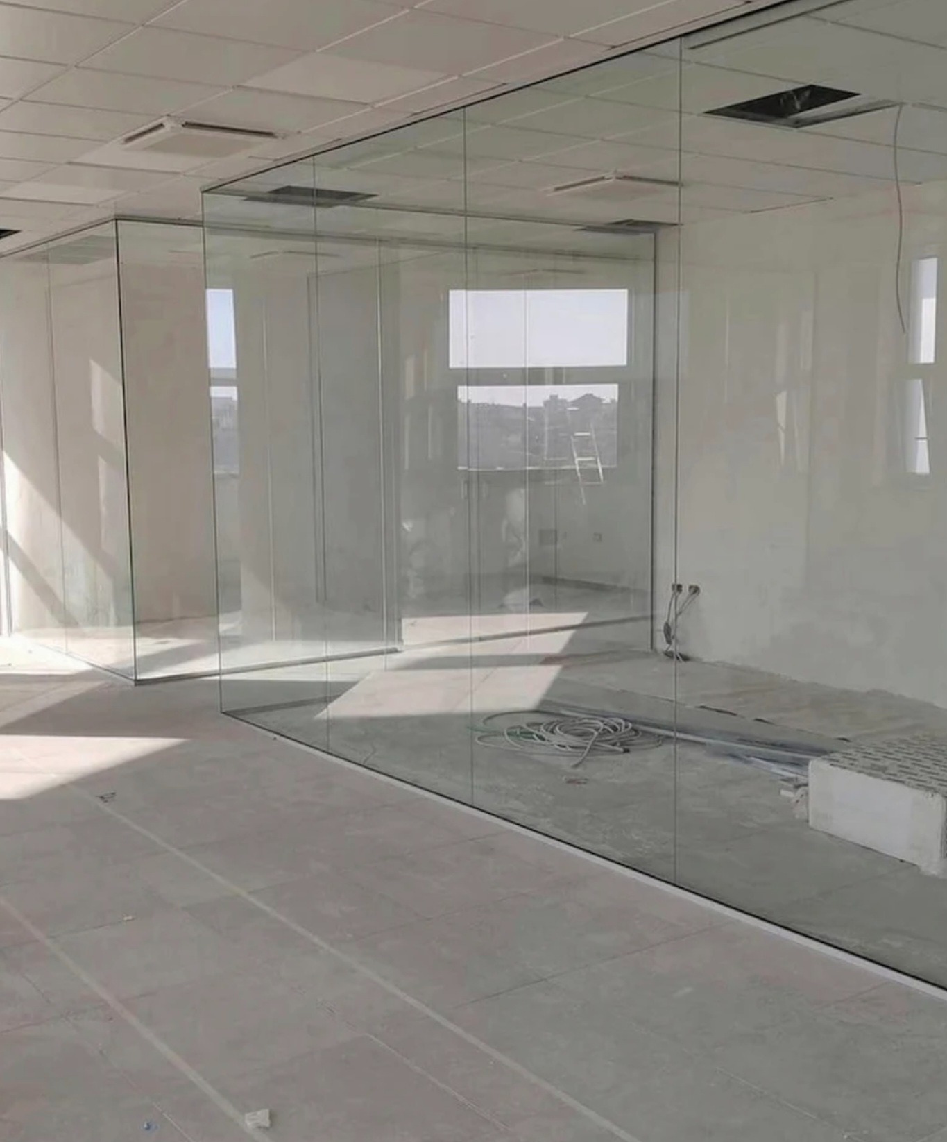 Szklane ścianki działowe w jasnym biurze, widoczne kable i elementy instalacji, sufit podwieszany z otworami. Minimalistyczny design, surowe wykończenie.