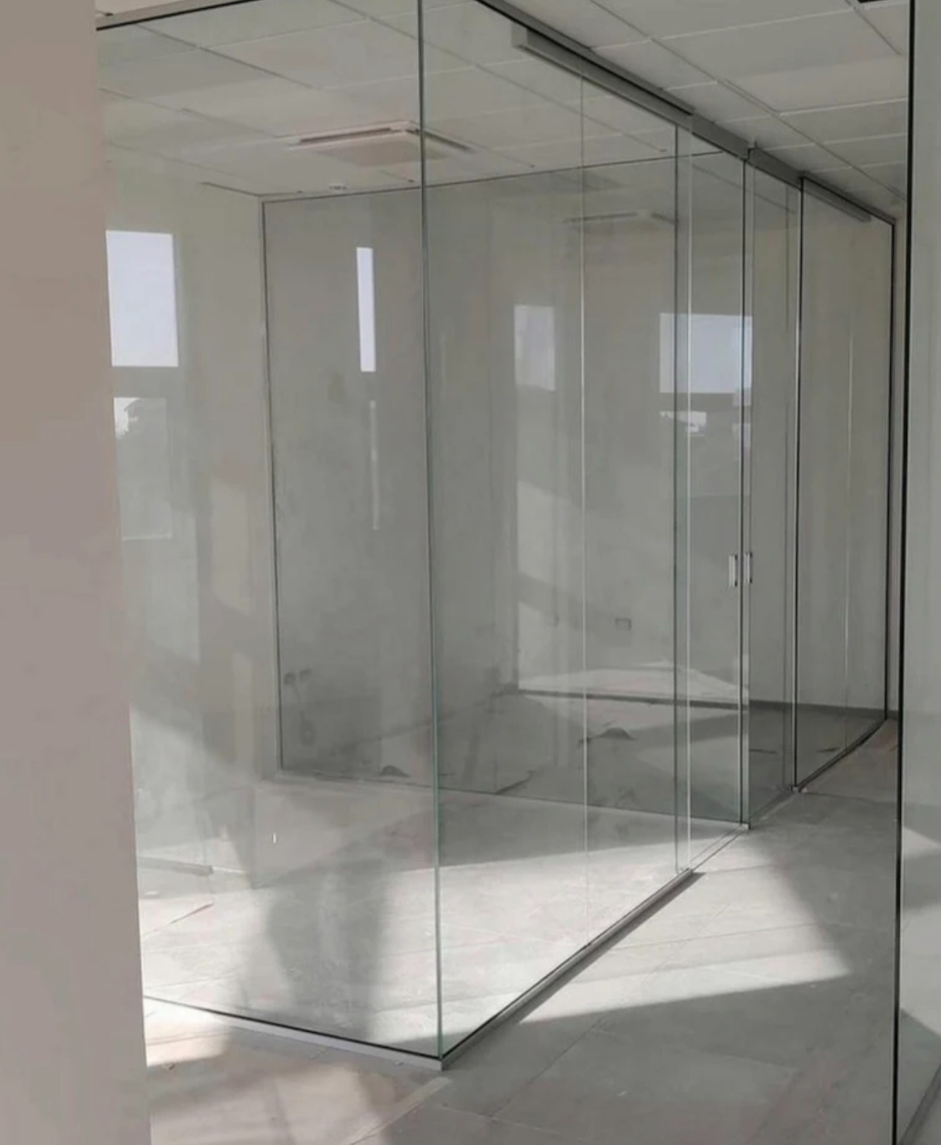 Szklana ścianka działowa z przesuwnymi drzwiami, widoczna w jasnym wnętrzu biurowym. Minimalistyczny design, metalowe prowadnice, subtelne uchwyty drzwiowe.