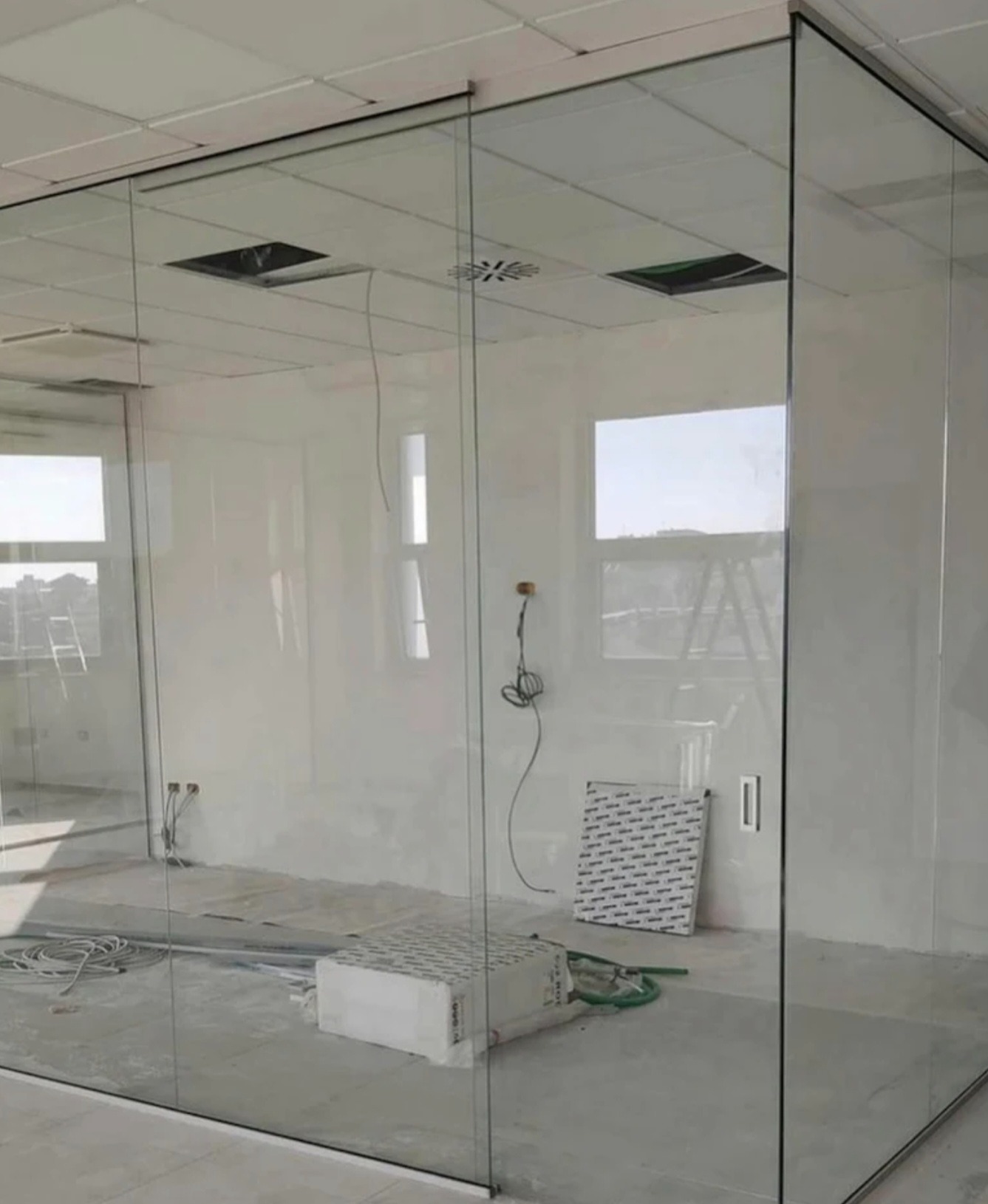 Szklana ścianka działowa w biurze, widoczne okna i elementy instalacji. Minimalistyczny design, surowy stan wykończenia wnętrza, jasne światło.