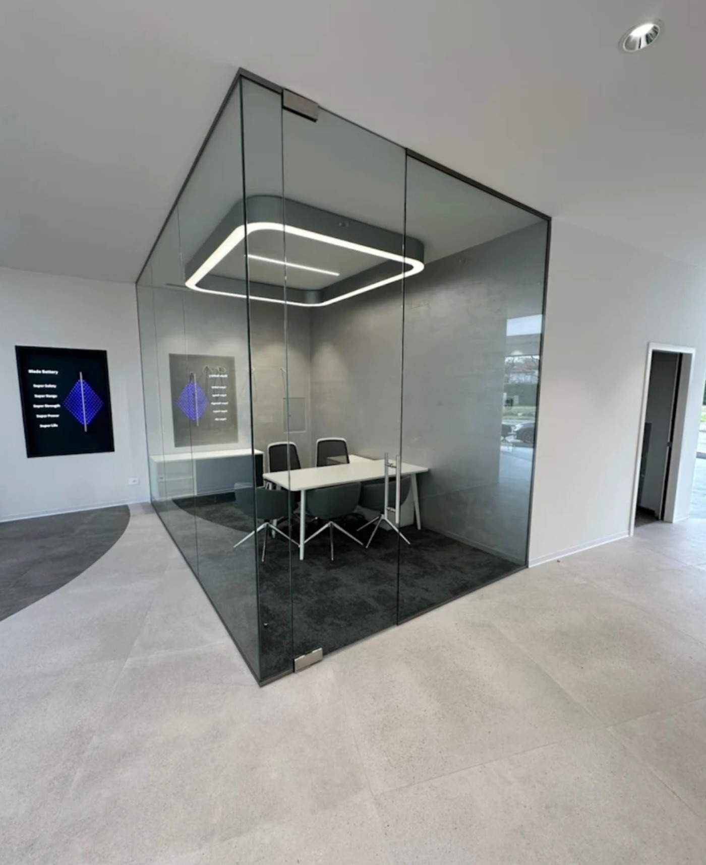 Szklana ścianka działowa tworząca nowoczesne biuro z oświetleniem LED. Minimalistyczny design, widoczne detale mocowań. Jasne wnętrze, neutralna kolorystyka.