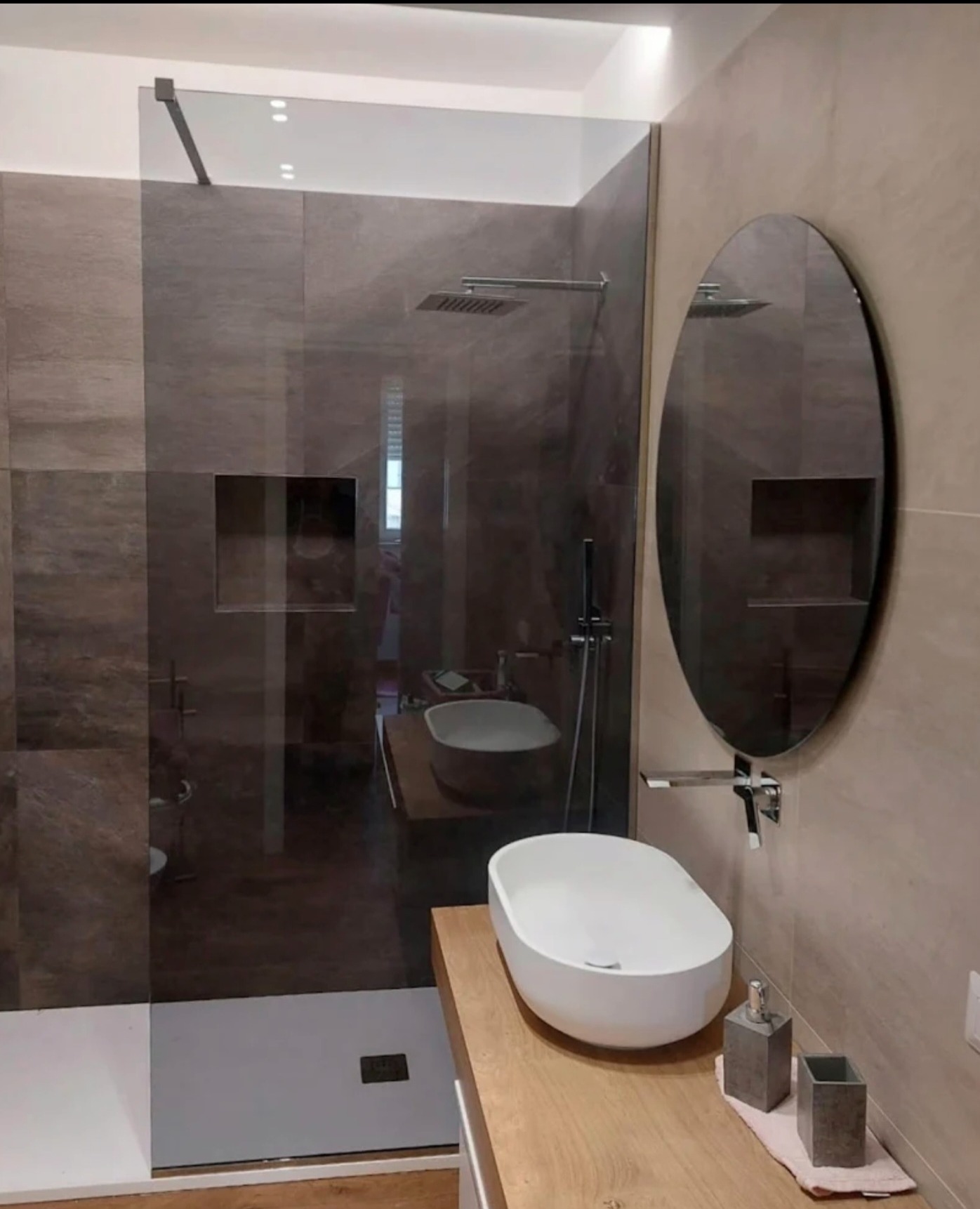 Nowoczesna łazienka z kabiną prysznicową typu walk-in, owalnym lustrem i umywalką nablatową. Minimalistyczny design, stonowana kolorystyka, eleganckie wykończenie.