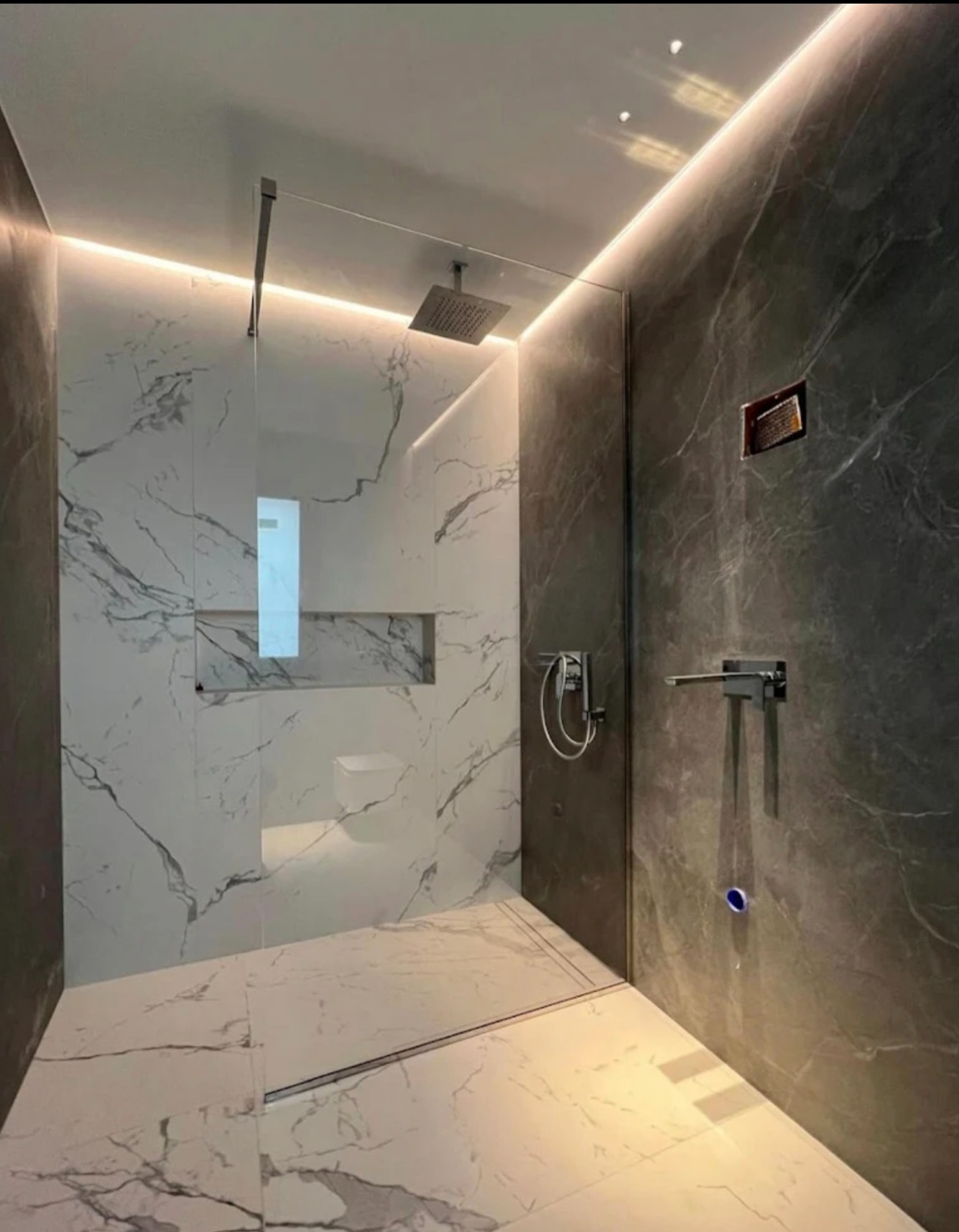 Nowoczesna kabina prysznicowa typu walk-in z marmurowymi płytkami i subtelnym oświetleniem LED, tworząca minimalistyczną i elegancką przestrzeń kąpielową.